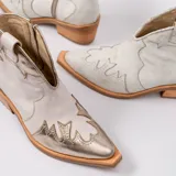 Botines de cuero vacuno color blanco con diseño bordado, taco de madera foliado en cuero de 5cm, cierre del lado interior y horma de punta fina.