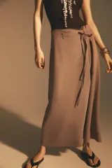 Falda midi color beige confeccionada en hilatura con viscosa. Tiene tiro alto, cintura con trabillas ajustable con lazada en el mismo tejido, detalle de doble pliegue en el delantero y bajo acabado con costuras marcadas a tono. Cierre lateral con cremallera oculta.