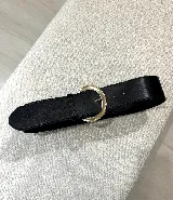 Cinturón ancho de cuero sintético negro con hebilla dorada en forma de media luna.