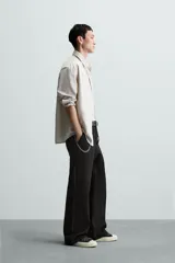 Pantalón negro de algodón con corte relajado y pierna ancha (flare fit). Presenta cierre frontal con botón y cremallera, bolsillos delanteros y bolsillos traseros de plastrón.