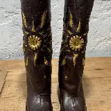 Bota de cuero marrón con bordado dorado en forma de sol.