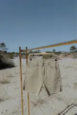 Bermuda de jean elastizado color beige, tiro alto, con dobladillo deshilachado y aberturas laterales en el ruedo.