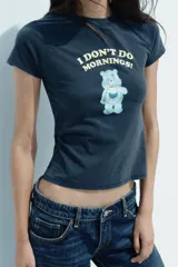 Remera azul de algodón con efecto lavado, cuello redondo y mangas cortas. Estampado frontal con un oso Care Bear y la frase "I don't do mornings!".