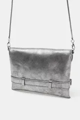 Bolso formato bandolera color plateado metalizado, con solapa frontal que simula un cinturón con hebilla metálica en forma de corazón. Posee asa fina de cadena y cierre mediante botón imantado.