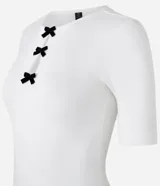 Blusa blanca de mangas cortas, confeccionada en Rib, con cuello redondo y lazos de terciopelo negros uniendo la abertura en la parte de abajo.