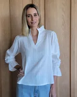 Blusa color beige con cuello con volados, mangas largas abullonadas con puños elásticos y cierre con botones en la parte delantera.