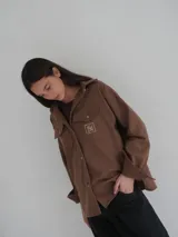 Camisa gris de lana con corte clásico, cuello camisero, cierre frontal con botones de cuerno y dos bolsillos de parche en el pecho.
