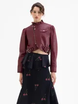 Chaqueta crop de cuero ovino color bordó, estilo biker, con cuello alto con volados y cierre metálico asimétrico. Presenta detalles de frunces en la copa de las mangas y volados en los puños.