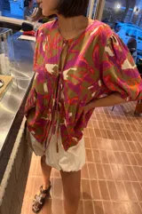 Blusa de calce holgado con estampado floral en tonos marrones, fucsias, naranjas y blancos. Escote en V con doble lazo ajustable y mangas 3/4 con volumen.
