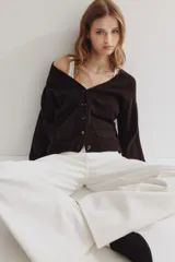 Cárdigan de punto suave color marrón oscuro, con cuello en V, botones frontales y bolsillos abiertos en la parte delantera. Presenta hombros caídos y remates acanalados en puños y bajo.