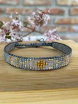 Pulsera tejida con cuentas Miyuki en tonos gris, dorado, plateado y rosa pálido. Cierre ajustable con cordón gris.