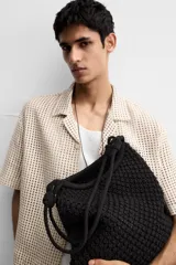 Bolso tipo shopper negro, confeccionado en tejido trenzado de algodón con diseño de red. Cuenta con dos asas de hombro ajustables que funcionan como cierre del compartimento principal.