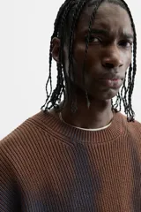Sweater marrón de punto con cuello redondo y manga larga. Tiene un estampado irregular con efecto spray en color azul.