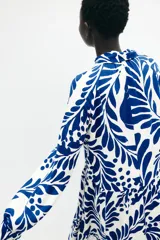 Vestido midi de viscosa con estampado floral azul sobre fondo blanco, cuello camisero, tapeta de botones oculta, mangas raglán largas con puños sencillos y costuras fruncidas en la falda.