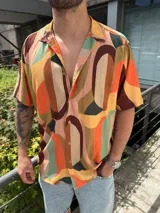 Camisa de hombre de manga corta con cuello clásico y cierre abotonado. Presenta un estampado abstracto con formas geométricas en tonos naranja, marrón, verde, beige y rosa.