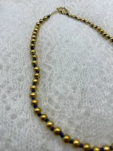 Collar corto de perlas doradas con hilo de seda azul marino y cierre de mosquetón dorado con cadena de extensión.