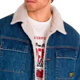 Chaqueta de denim azul con forro de sherpa color crema, cierre con botones metálicos, bolsillos superiores con broche metálico, bolsillos inferiores tipo Welt y puños con cierre sin marca.