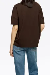 Camiseta oversize de algodón y poliéster color crema con escote redondo y mangas cortas anchas. Presenta un bordado frontal con hilos colgantes de colores variados.