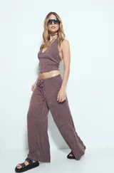 Pantalón de tiro bajo, calce relajado y pierna amplia, color marrón oscuro con textura acanalada. Presenta cintura ajustable con lazo.