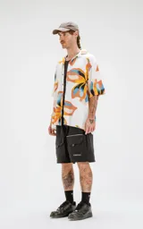 Camisa de manga corta con estampado floral en tonos amarillos, naranjas, azules y marrones sobre fondo blanco. Calce oversize y canesú en la espalda.