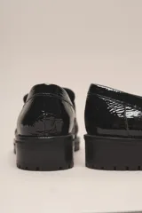 Mocasín negro de cuero vacuno con acabado charol, suela de goma y forro y plantilla de cuero vacuno.