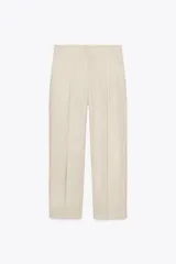 Pantalón color crema de lino, de tiro alto con pinzas delanteras, bolsillos laterales y falsos bolsillos traseros de vivo. Cierre frontal con cremallera, botón interior y gancho.