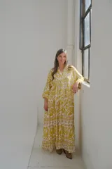 Vestido largo amarillo con estampado floral blanco, cuello en V, mangas 3/4 y corte escalonado.