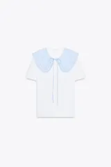 Camiseta blanca de manga corta con cuello bobo de tela a cuadros vichy celeste y blanco con bordes bordados. El cuello tiene lazos finos del mismo tejido.