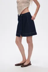 Minifalda de jean azul oscuro con corte evasé, cierre frontal cruzado con botón y detalle de costuras a contraste.