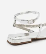 Sandalia plana plateada con tiras finas y detalles de strass, puntera cuadrada y cierre con hebilla en el tobillo.