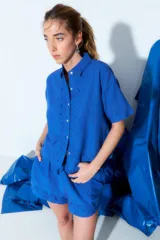 Camisa celeste de manga corta con cuello clásico, cierre frontal con botones y bordados ondulados en el frente.