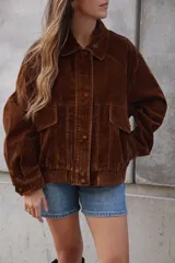 Campera estilo bomber marrón oscuro, confeccionada en tela de pana o terciopelo, con cuello camisero, cierre frontal de botones y puños y cintura acanalados.
