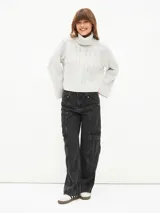 Polerón de tejido de punto color gris claro, con cuello alto y diseño de trenzas en el cuerpo y mangas. Corte holgado y puños anchos.