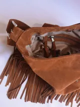 Bolso tipo bandolera de cuero negro con flecos y tachas plateadas. Tiene correa regulable, forro interior y bolsillo interno.