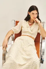 Top corto cruzado color crema con estampado de puntos dorados, escote en V con volados y mangas abullonadas al codo con puños elastizados.