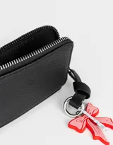 Monedero negro de cuerina con cierre circundante y charm colgante de moño rojo y torre Eiffel plateada.