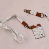 Llavero tipo cinta para colgar al cuello, con estampado de estrellas en tonos verde menta y blanco. Incluye un terminal de cuero sintético marrón con logo grabado y un gancho metálico de color bronce.