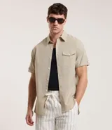 Camisa de hombre de manga corta en lino color blanco, con cuello clásico, botonadura frontal y bolsillo de parche en el pecho. Corte recto.