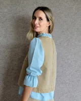 Chaleco blanco con cuello redondo y sisas amplias. Presenta costuras verticales a la vista y un bolsillo lateral con detalle de costura en forma de equis.