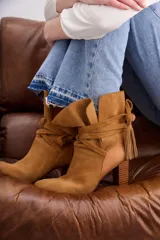 Botas de caña media color marrón, confeccionadas en gamuza, con taco de madera y punta fina. Presentan tiras del mismo material que se cruzan y atan alrededor de la caña, terminadas con borlas.