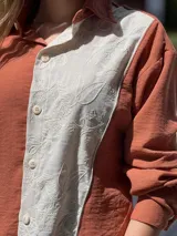 Camisa oversize color crema, de manga larga confeccionada en mezcla de lino y algodón. Presenta diseño bicolor con panel frontal bordado, cartera de botones y cuello clásico.