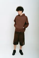 Bermuda de jean color marrón con lavado gastado, corte baggy, bolsillos grandes y bordados ornamentales en los laterales.