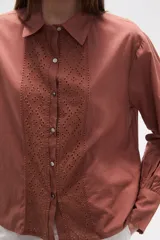 Camisa blanca de broderie con cuello camisero, cierre frontal de botones, mangas largas y corte holgado.