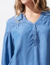 Blusa celeste de lyocell con cuello a la base y escote en V con apertura central y botones. Manga ¾ con puño y botón.