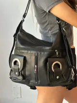 Cartera bandolera negra con múltiples bolsillos frontales con cierre y hebillas decorativas.