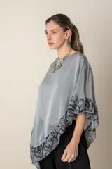 Blusa tipo poncho color gris con zócalo de tul bordado con motivos florales negros. Incluye una camiseta interior de spandex.