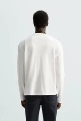 Camiseta blanca de manga larga con cuello redondo y textura cuadriculada.