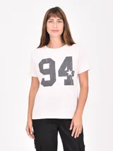 Remera de manga corta color rosa pálido con cuello redondo y un gran estampado frontal de los números "94" y una estrella en gris oscuro con efecto desgastado.