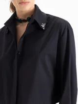 Camisa blanca de poplin de algodón con fit cómodo y largo que cubre hasta debajo de la cintura. Presenta botones ocultos en cartera y puños, y punteras de níquel en el cuello.