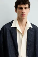 Blazer azul oscuro de denim, corte relaxed fit, con cuello de solapas de muesca, manga larga con puños abotonados, bolsillos de solapa en la cadera, abertura en el centro de la espalda y cierre frontal con botones.